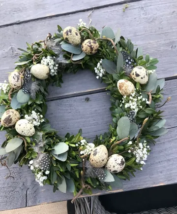 Wreath with eggs and flowers on table.