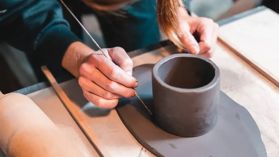 Person crafting cylindrical clay pot indoors.