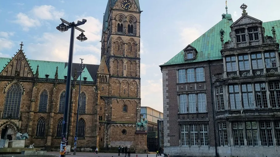 Historic buildings with clock tower, cloudy sky.