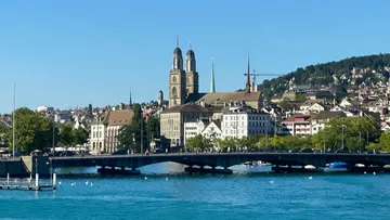 Brücke über Fluss, Stadt und Hügel im Hintergrund.