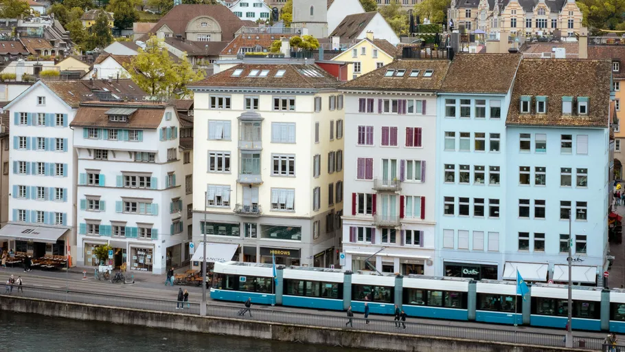 Tram passing by colorful riverside buildings.