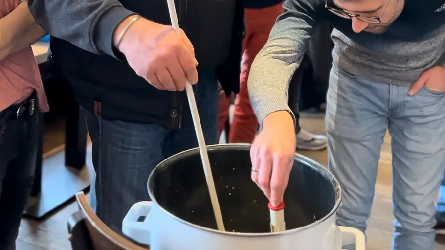 Two people stirring a large pot indoors.