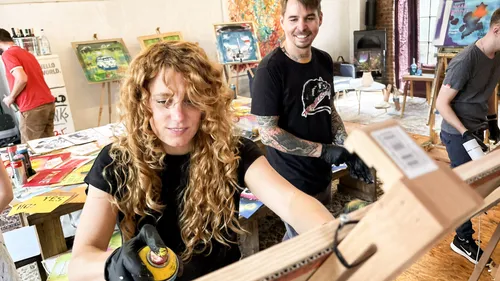 Woman paints on easel; people around her.