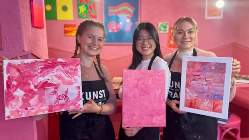 Three women showing pink abstract paintings.