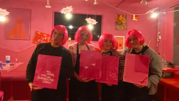 Vier Personen halten Gemälde, tragen pinke Perücken.