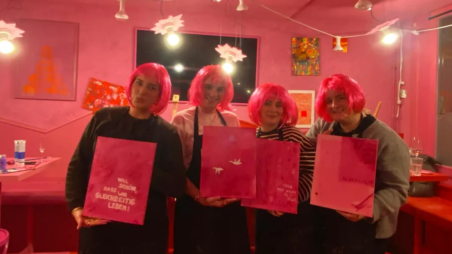 Four people holding paintings, wearing pink wigs.