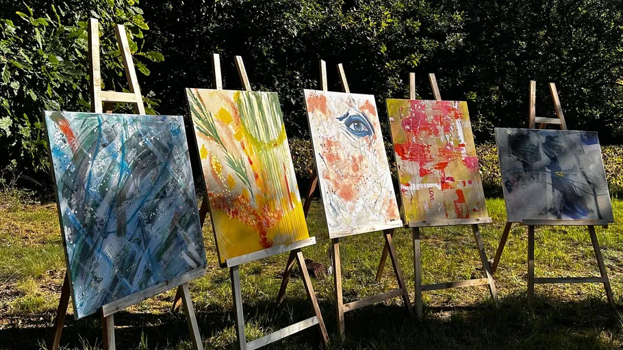 Five abstract paintings on easels outdoors.