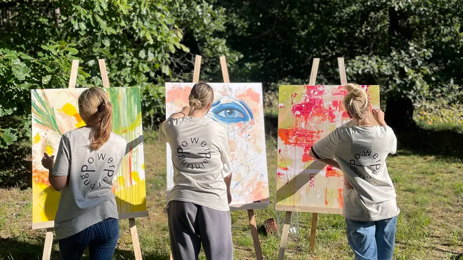 Three people painting on easels outdoors.