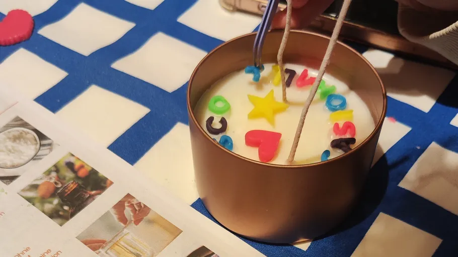 Hand placing letters in wax for candle making.