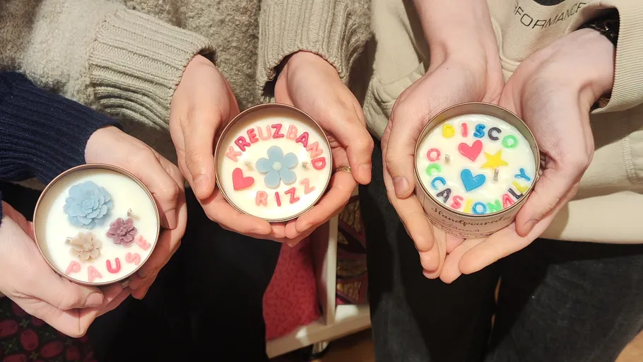 Three hands holding decorative candles indoors.