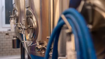 Stainless tanks with blue hoses in brewery.