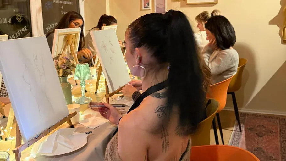 Women painting on canvases in decorated room.