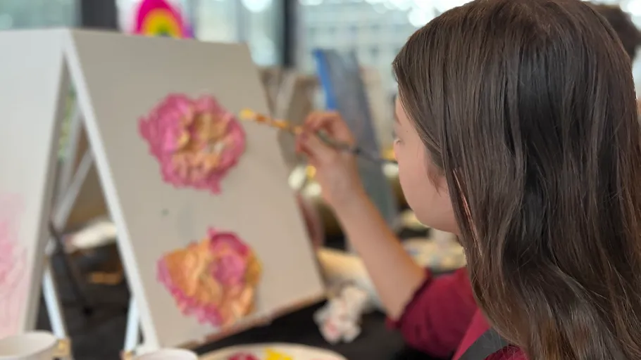 Person painting flowers on a canvas indoors.