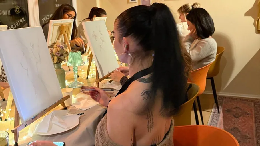 Women painting at canvases in a cozy room.