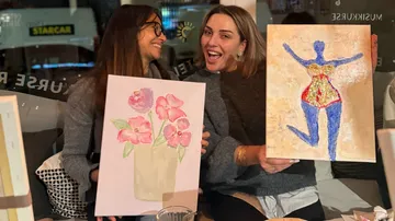 Two women smiling, holding their paintings.