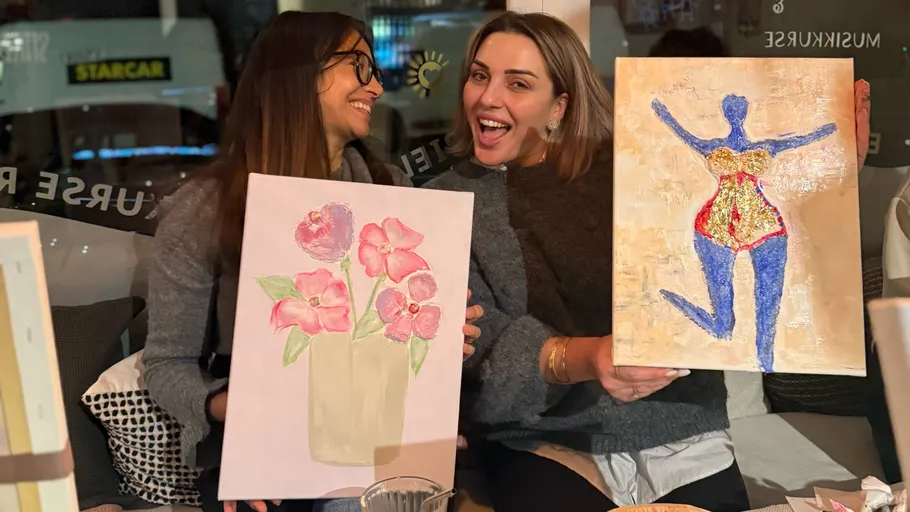 Zwei Frauen lächeln, halten ihre Gemälde.