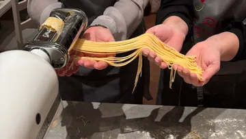 Hands holding fresh pasta near machine.