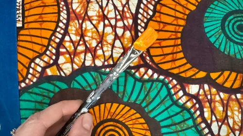 Hand holding paintbrush over colorful fabric.