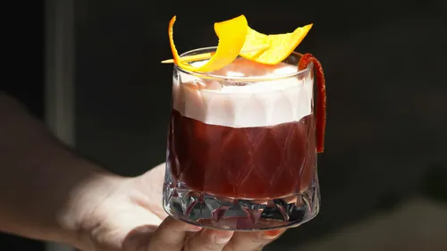 Glass of cocktail with orange peel garnish.