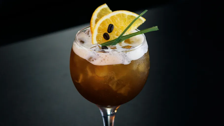 Orange garnish on iced cocktail glass, dark background.