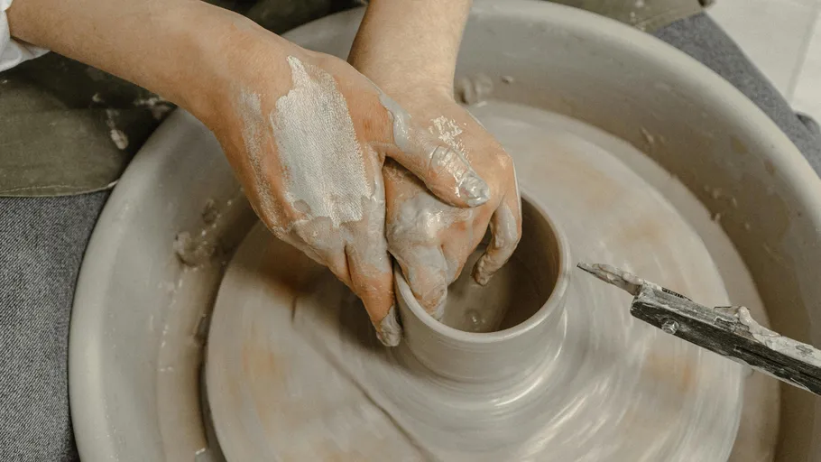 Hands shaping clay on pottery wheel.