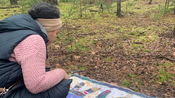 Person sitzt auf Decke im Wald.