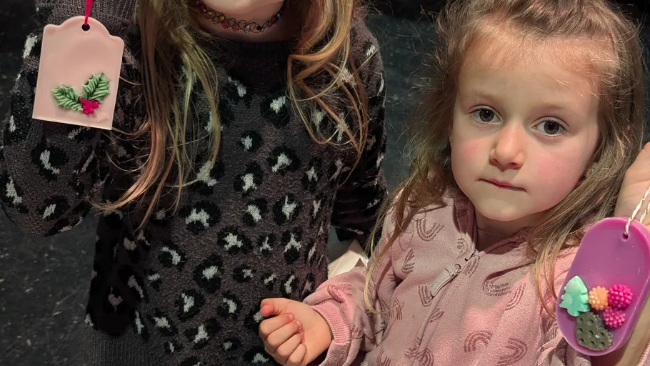 Two girls holding decorated ornaments indoors.