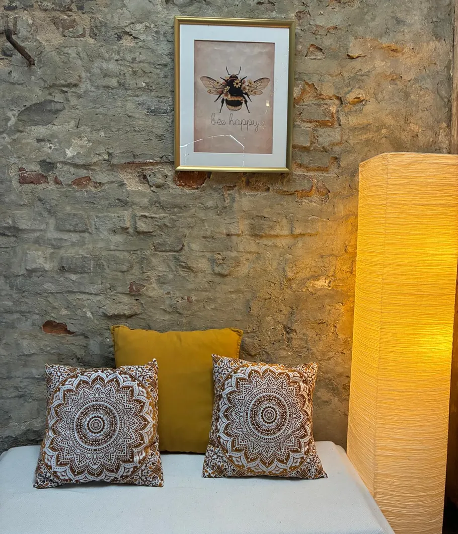 Gemütliche Ecke mit Kissen, Lampe und Bienenbild.