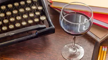 Alte Schreibmaschine, Weinglas, Notizbücher auf Tisch.