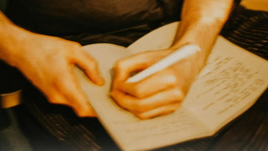 Person schreibt in Notizbuch auf dem Schoß.