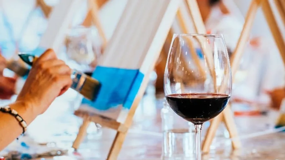 Person painting with blue near wine glass.