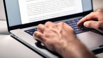 Hands typing on laptop keyboard indoors.