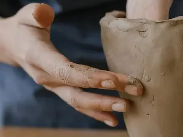 Hand form a clay pot on a workbench.