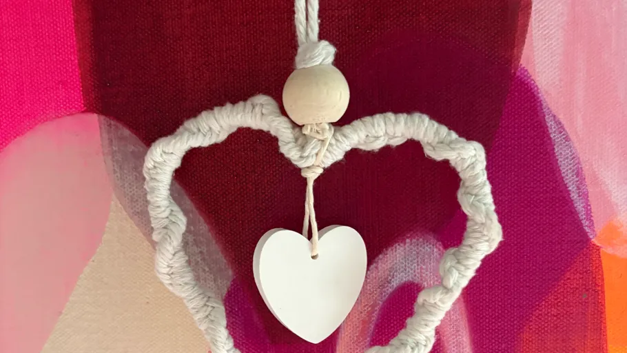 Macramé heart with hanging heart on colorful background.