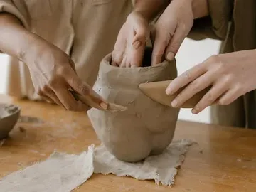 Hands form a clay pot on a wooden table.