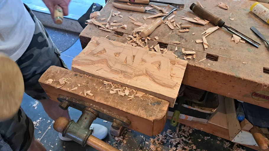 Wood carving process on workbench, person using tools.