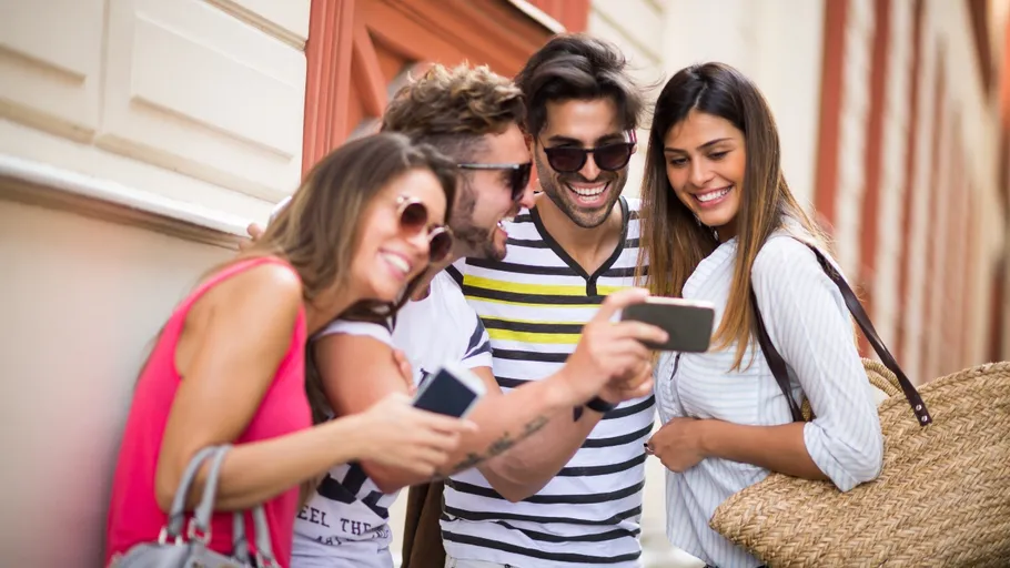 Four friends smiling at smartphone outdoors.
