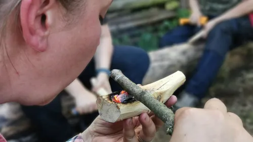 Person starts fire using wood friction outdoors.