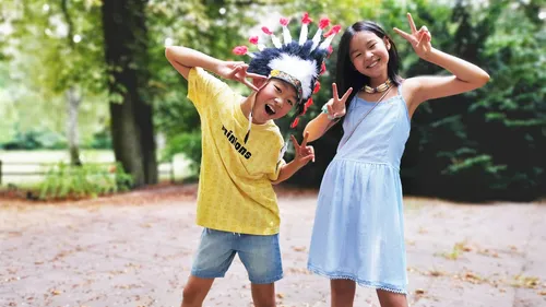 Zwei Kinder posieren draußen mit Peace-Zeichen.