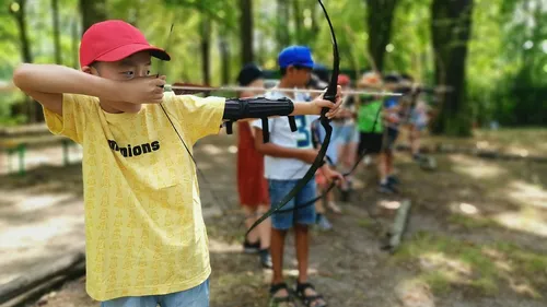 Child aiming bow in forest with others.