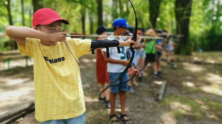 Child aiming bow in forest with others.