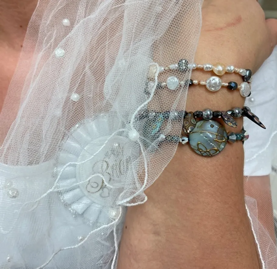 Hand mit Armbändern unter dekorativem Stoff.