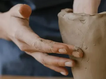 Hands form a clay container in a workshop.