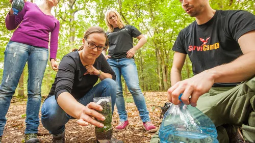 People examining bottles in a forest setting.
