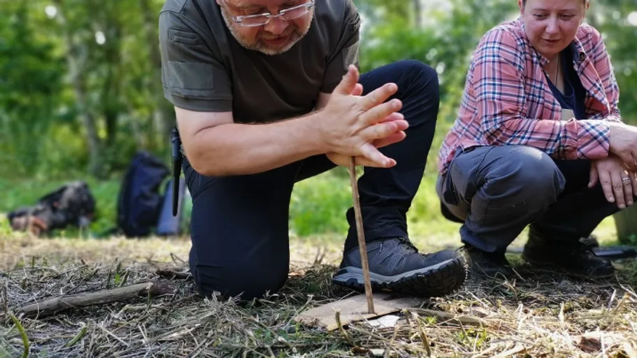 Two people making fire with wood in forest.