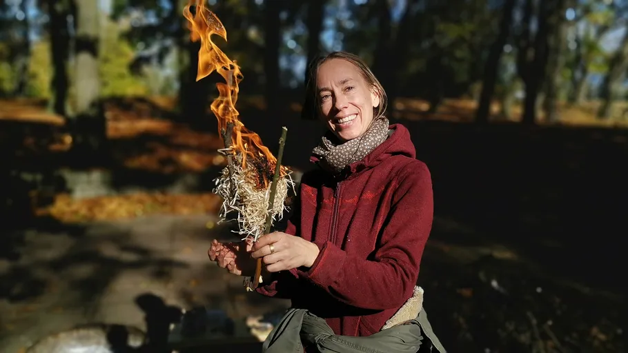 Person holding flaming stick in forest.