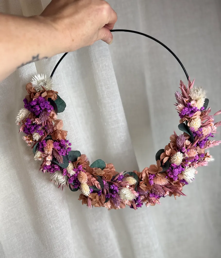 Hand hält Kranz mit Trockenblumen.