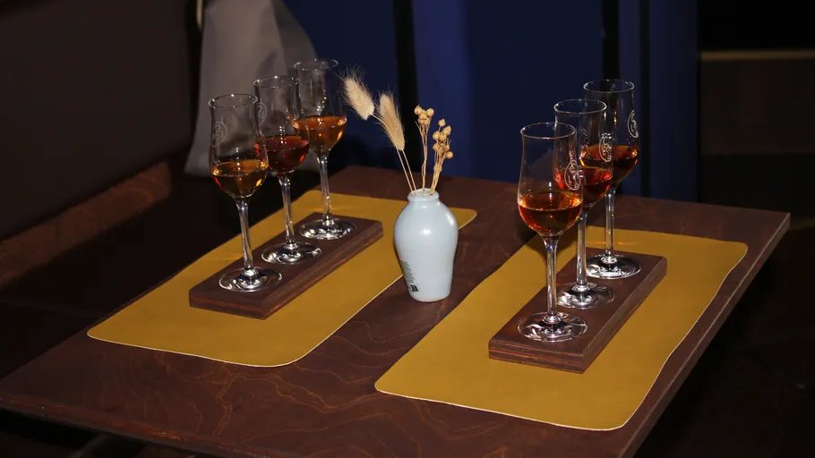 Glasses of amber liquid on wooden trays, table.