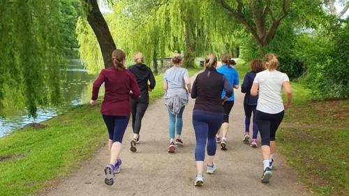 Gruppe joggt auf Parkweg, umgeben von Bäumen.