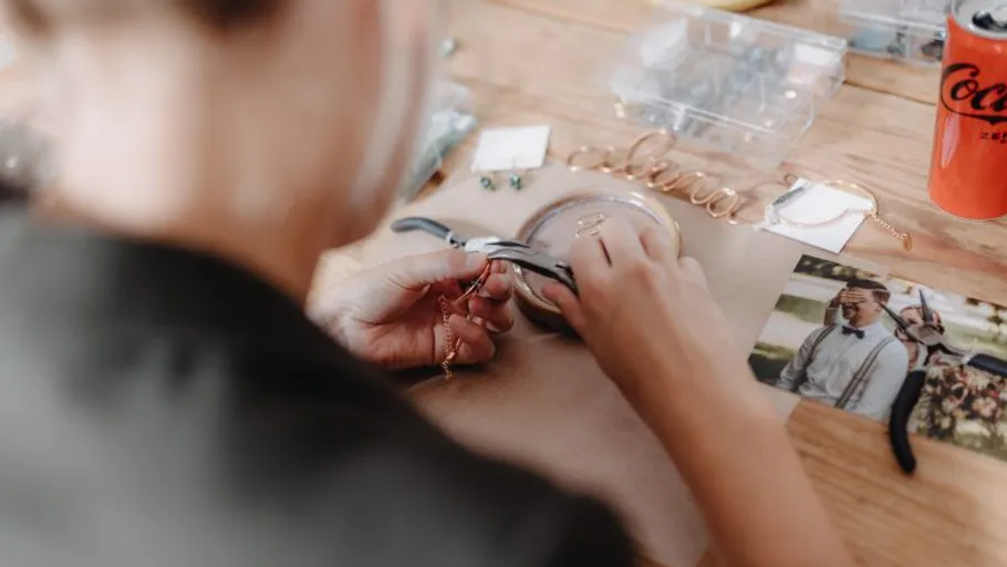 Person crafting jewelry on wooden table.